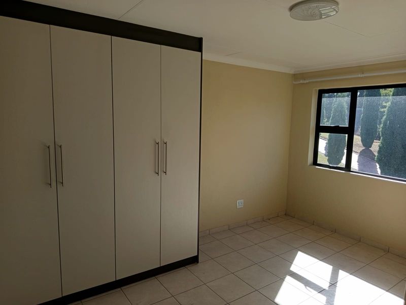A bright, empty bedroom featuring neutral tiled flooring, built-in cupboards, and a large window providing natural light.