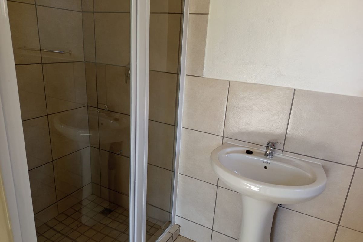 A functional bathroom featuring a pedestal basin, tiled walls and flooring, and a glass-enclosed shower unit.