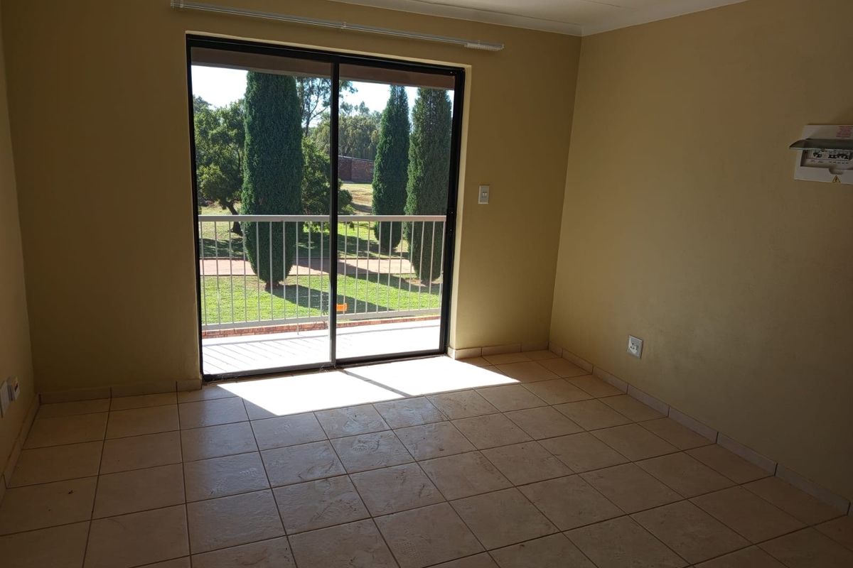 An empty living room featuring tiled flooring and a sliding glass door that opens onto a balcony with garden views.