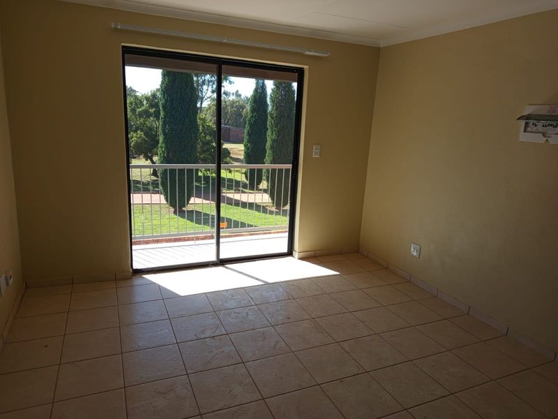 An empty living room featuring tiled flooring and a sliding glass door that opens onto a balcony with garden views.