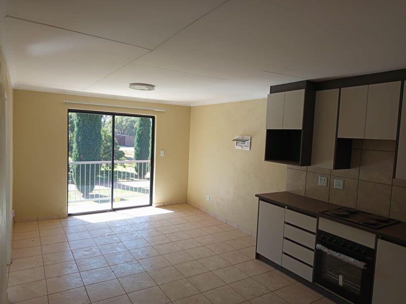Open-plan living area featuring tiled flooring, a built-in kitchen with cabinetry and appliances, and a sliding door leading to an outdoor balcony.