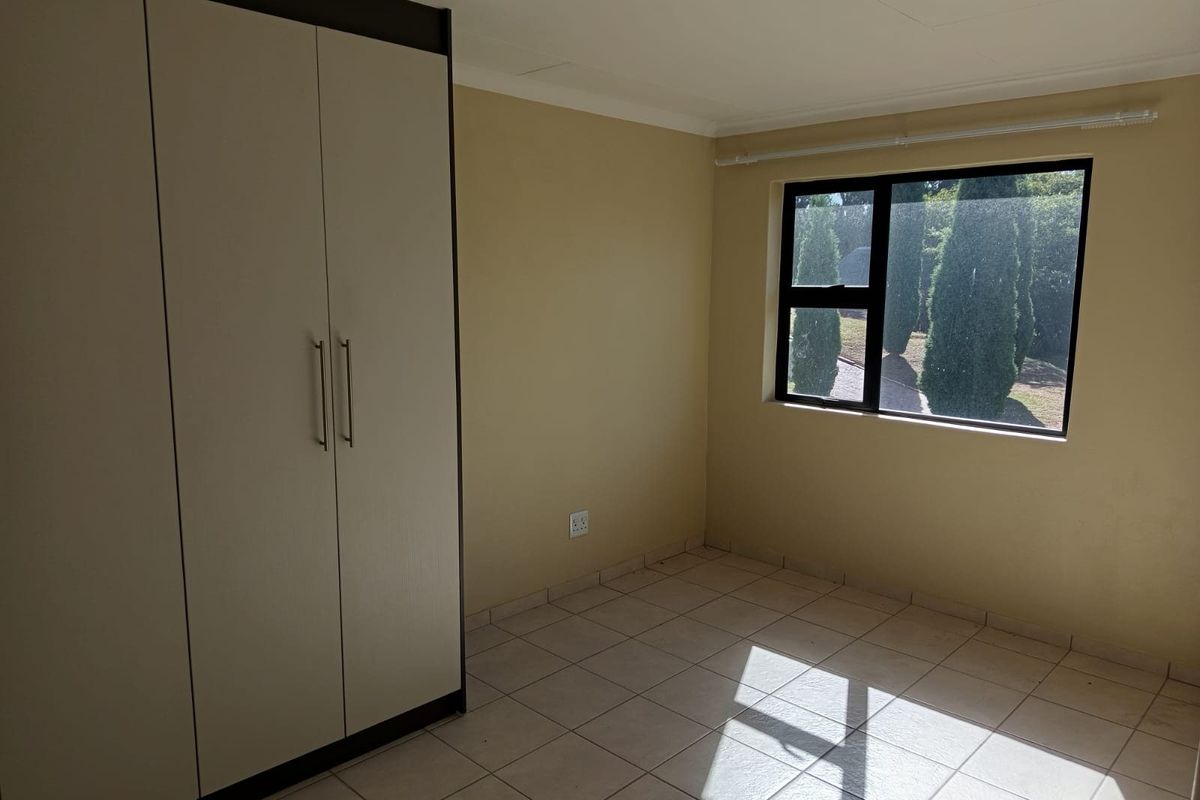 A bright, empty bedroom featuring neutral tiled flooring, a built-in wardrobe, and a large window providing natural light.