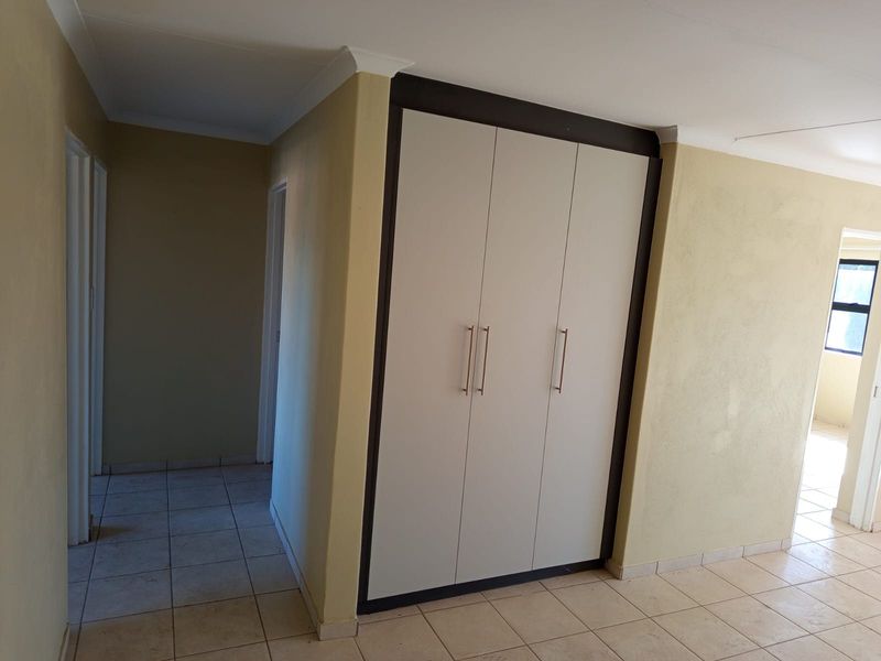 A clean, empty hallway featuring neutral tiled flooring and built-in storage cupboards with modern handles.