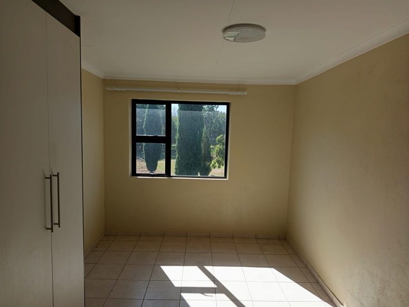 A vacant bedroom featuring tiled flooring, a built-in wardrobe, and a window with a garden view.