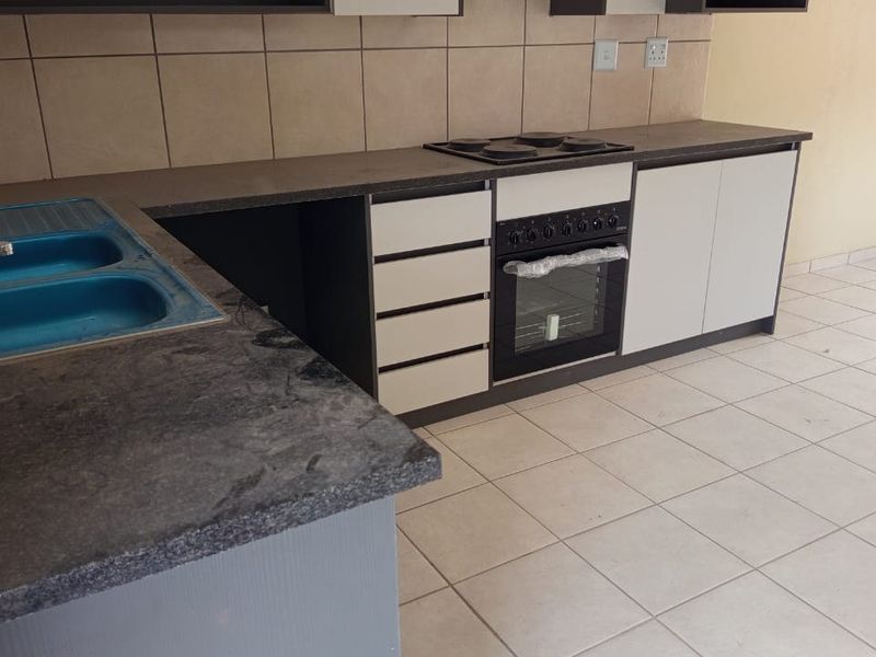 A functional kitchen featuring built-in cabinetry, a double sink, an integrated oven with an electric hob, and tiled flooring throughout.