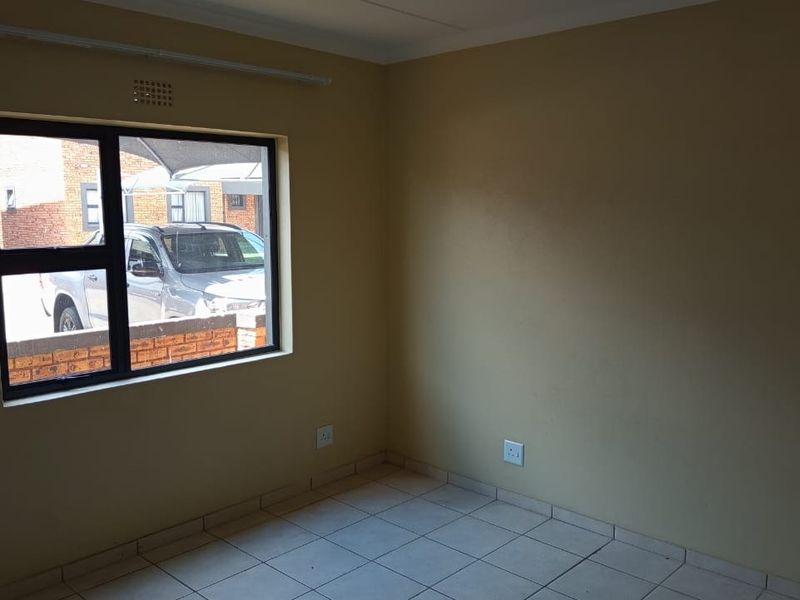 A vacant bedroom featuring tiled flooring, neutral wall paint, and an aluminium-framed window providing natural light.