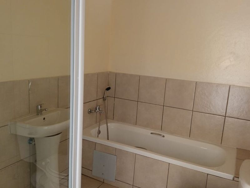 A functional bathroom featuring a bathtub, shower enclosure, and pedestal basin with neutral wall tiling.
