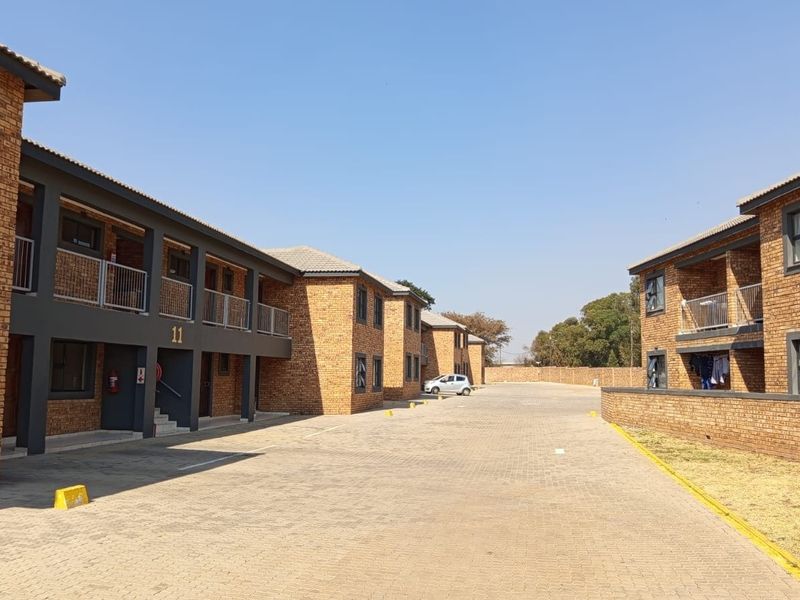 Exterior view of a multi-story apartment complex featuring face brick construction, paved driveway, and private balconies with metal railings.