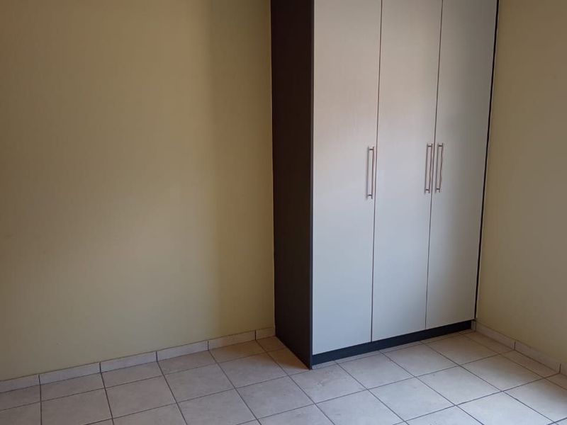 A clean, empty bedroom featuring neutral wall tones, tiled flooring, and a modern built-in wardrobe with ample storage space.