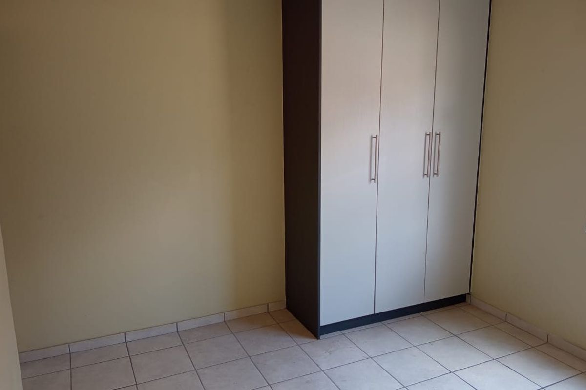 A clean, empty bedroom featuring neutral wall tones, tiled flooring, and a modern built-in wardrobe with ample storage space.