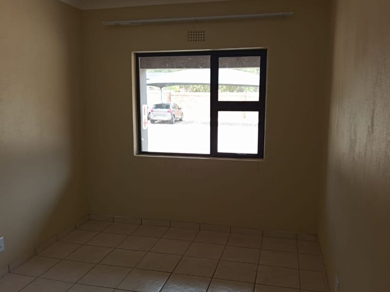 An empty bedroom featuring tiled flooring and an aluminium window frame, providing a neutral canvas for personalization.