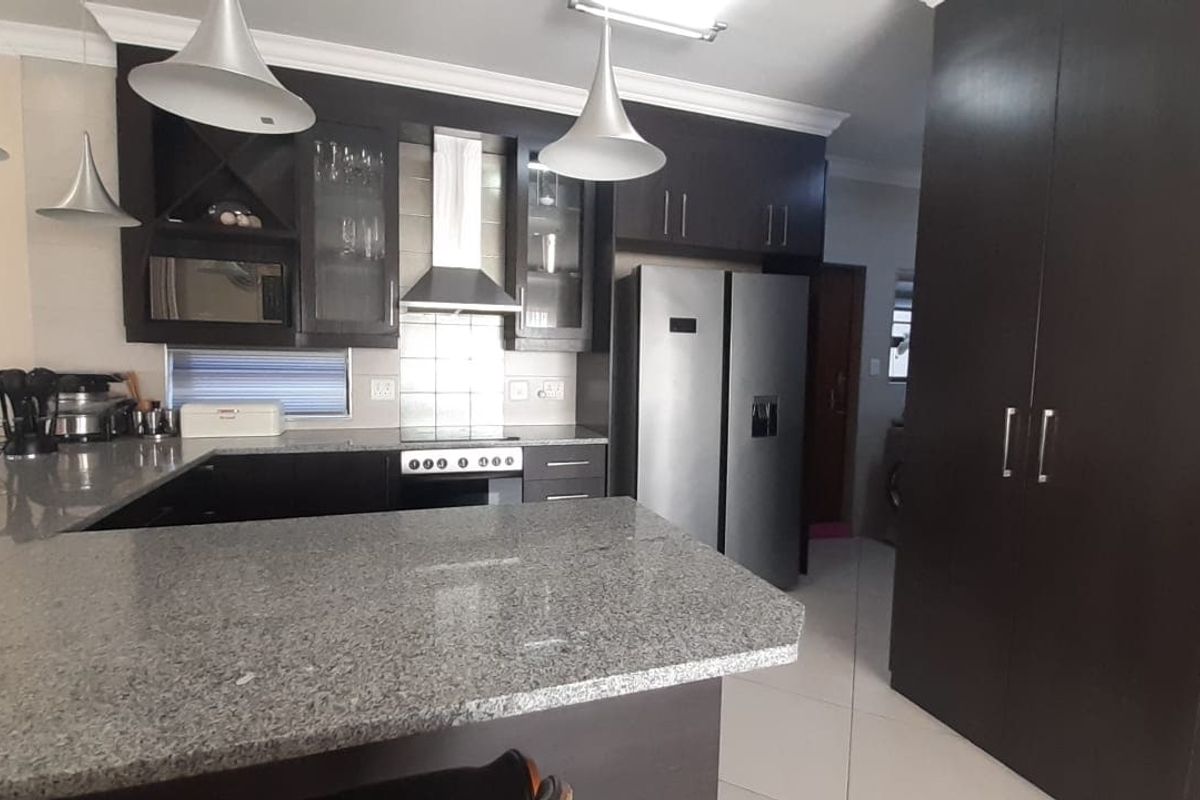 Modern kitchen featuring dark cabinetry, granite countertops, integrated appliances, and tiled flooring with a breakfast bar area.