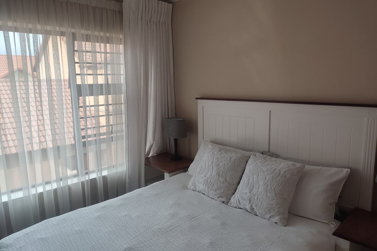 A well-maintained bedroom featuring a built-in headboard and large window with curtain tracks, offering a comfortable and functional living space.