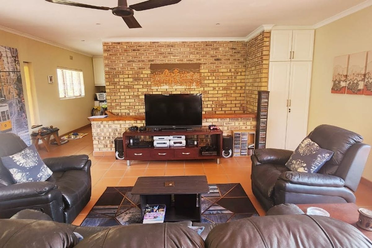 Spacious living room featuring an exposed brick wall, built-in storage cabinetry, tiled flooring, and a ceiling fan, offering a comfortable and functional living space.