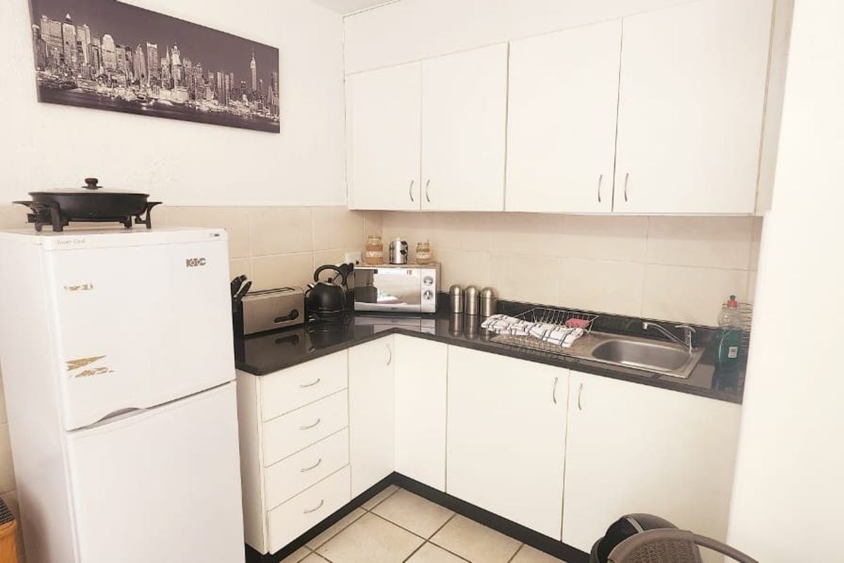 Compact kitchen featuring white cabinetry, dark countertops, tiled backsplash, and tiled flooring, providing a functional and efficient workspace.