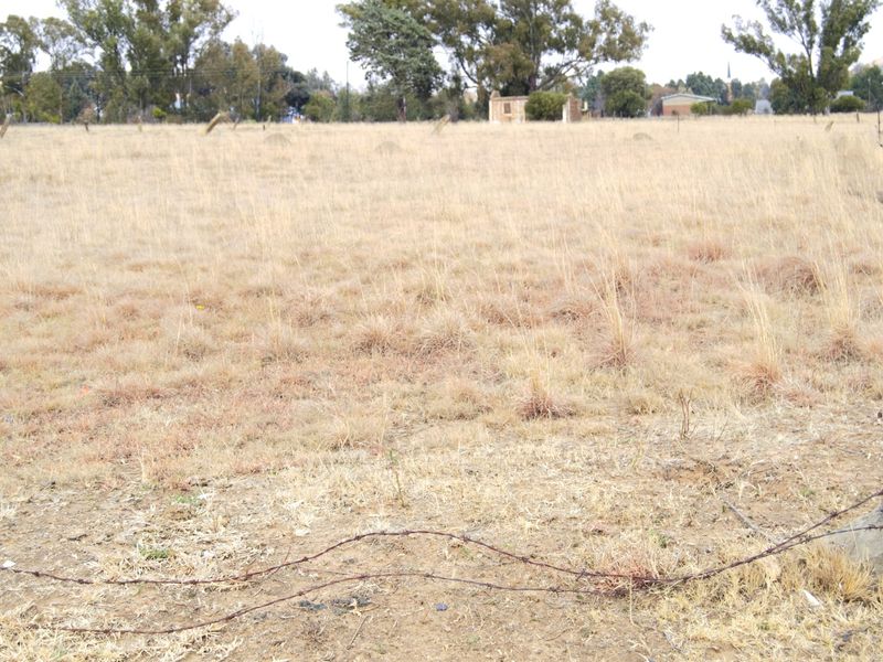 A vacant residential plot featuring dry grass and perimeter barbed wire fencing, offering a clear view of the surrounding landscape.