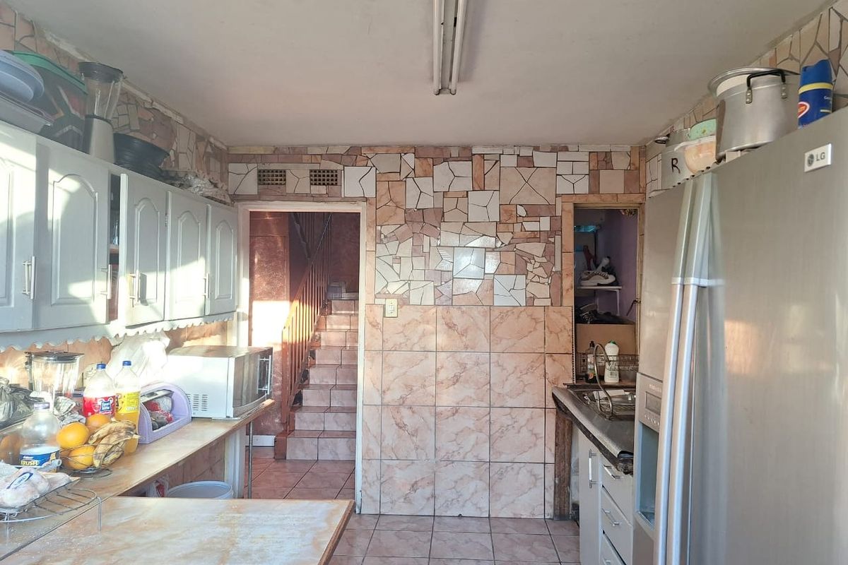 A dated kitchen featuring tiled walls, built-in cabinetry, and a stainless steel sink, with an adjacent staircase visible in the background.