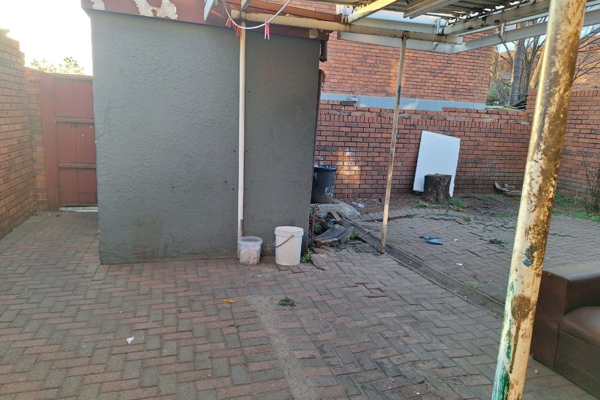 A rear courtyard area featuring brick paving, a metal carport structure, and brick boundary walls, requiring maintenance and cosmetic updates.