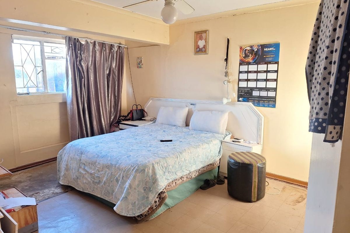A bedroom featuring a built-in headboard, ceiling fan, and security bars on the window, requiring cosmetic updates to the flooring and wall finishes.
