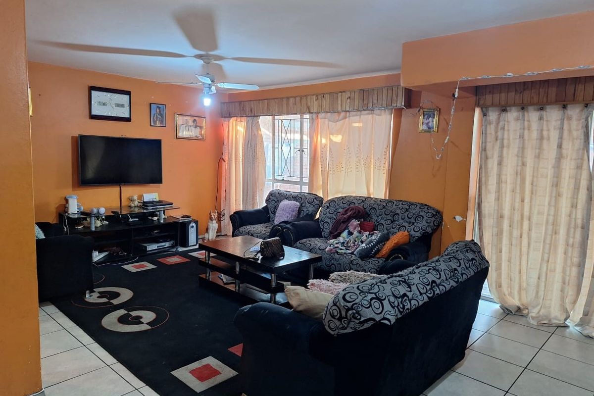 Spacious living room featuring tiled flooring, a ceiling fan, and large windows with security gates, offering a functional layout ready for modern updates.