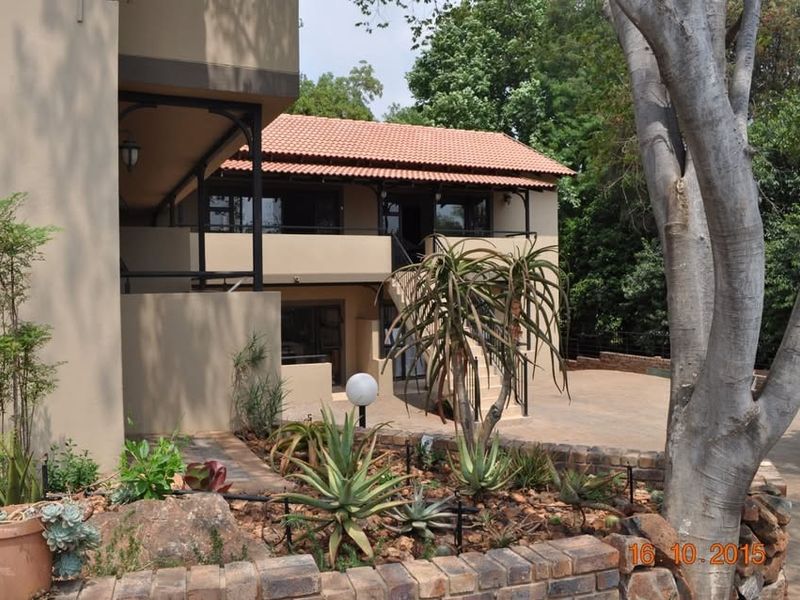 Rear view of the apartment building featuring a covered balcony, external staircase, and landscaped garden area with a brick retaining wall.