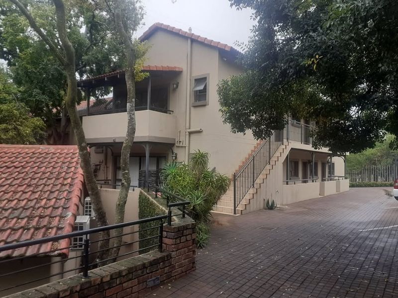 Exterior view of a multi-level apartment building featuring terracotta roof tiles, an external staircase, and a paved driveway area.