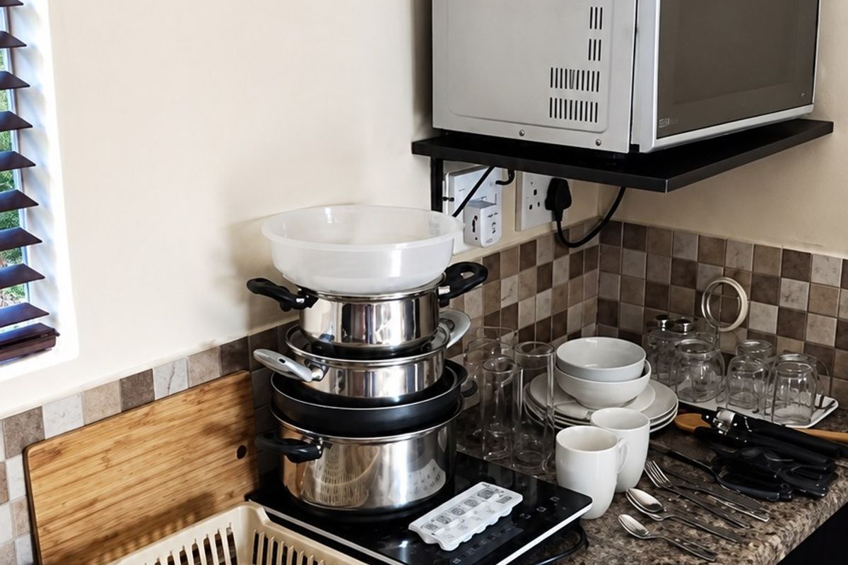 A compact kitchen area featuring granite countertops, dark wood cabinetry, a tiled backsplash, and a stainless steel sink with integrated prep space.