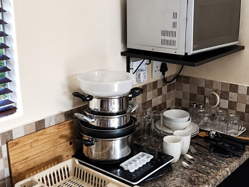 A compact kitchen area featuring granite countertops, dark wood cabinetry, a tiled backsplash, and a stainless steel sink with integrated prep space.