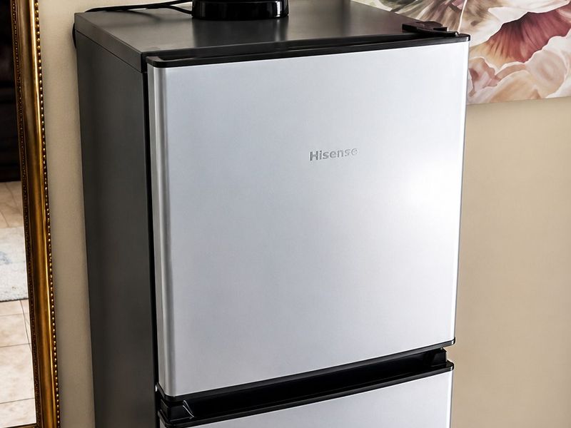 A compact kitchen area featuring tiled flooring and skirting boards, currently housing a freestanding refrigerator.