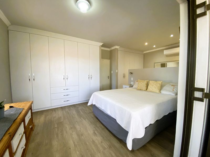 Spacious bedroom featuring extensive built-in wardrobes, modern laminate flooring, recessed lighting, and a wall-mounted split-system air conditioner for climate control.