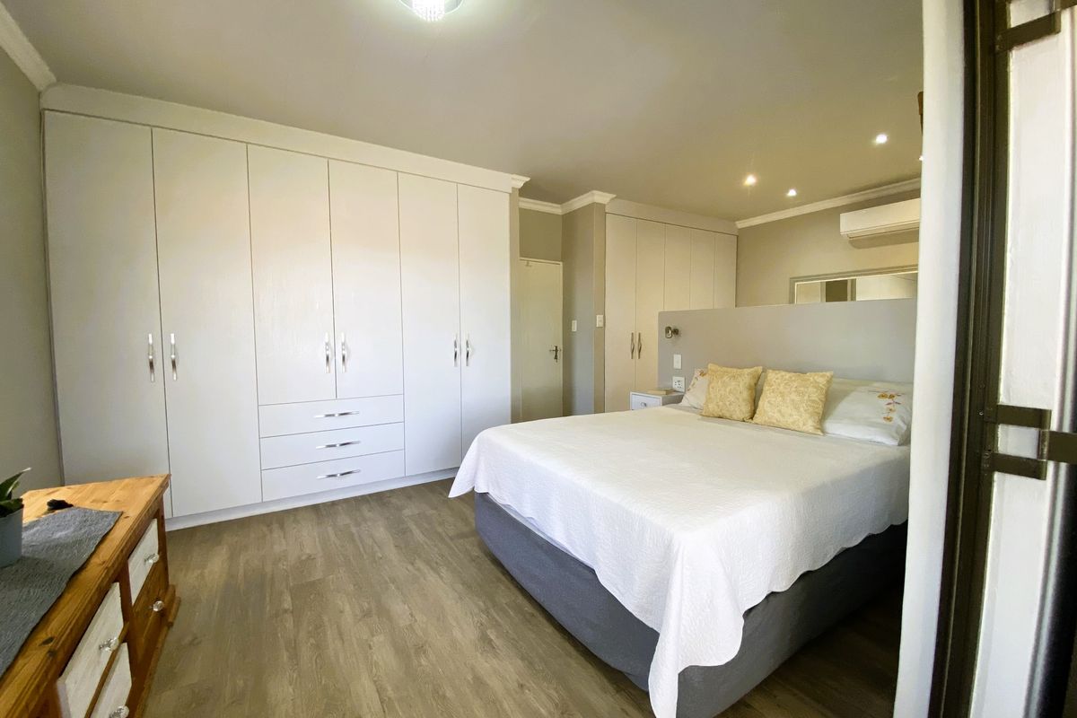 Spacious bedroom featuring extensive built-in wardrobes, modern laminate flooring, recessed lighting, and a wall-mounted split-system air conditioner for climate control.