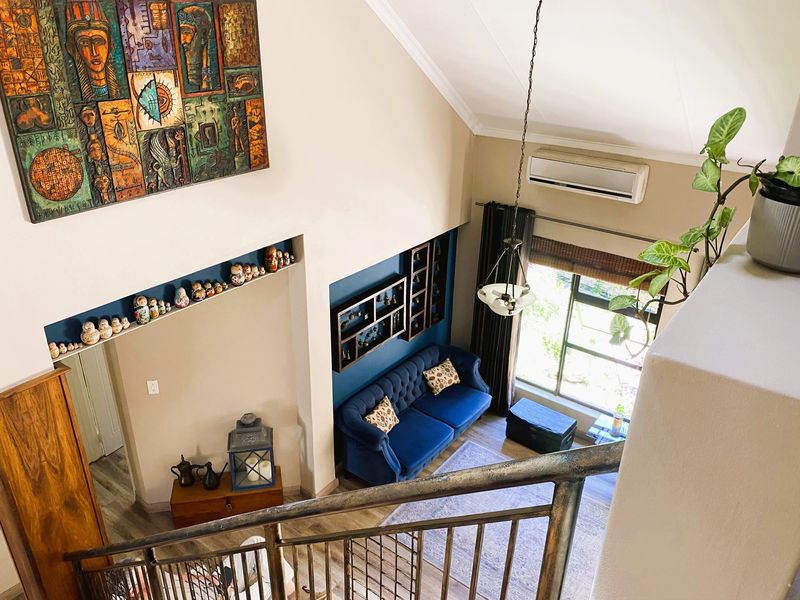 A high-ceilinged living room viewed from above, featuring a split-system air conditioner, recessed shelving, and a metal staircase railing.
