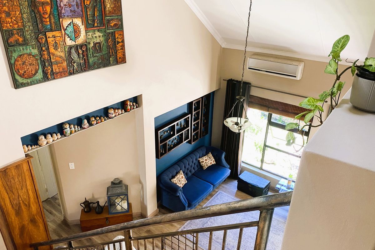 A high-ceilinged living room viewed from above, featuring a split-system air conditioner, recessed shelving, and a metal staircase railing.