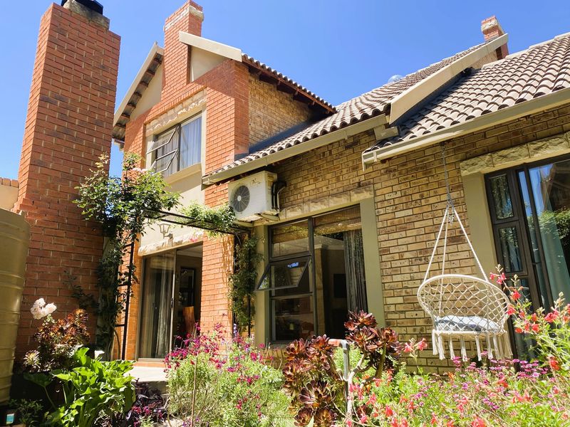 Rear elevation of a brick house featuring a prominent chimney, tiled roof, air conditioning unit, and established garden with sliding door access.