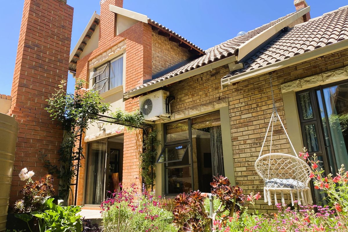 Rear elevation of a brick house featuring a prominent chimney, tiled roof, air conditioning unit, and established garden with sliding door access.