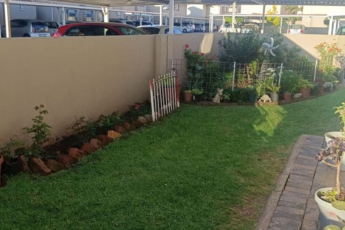 A private rear garden area featuring a manicured lawn, perimeter boundary wall, and paved walkway adjacent to the apartment building.