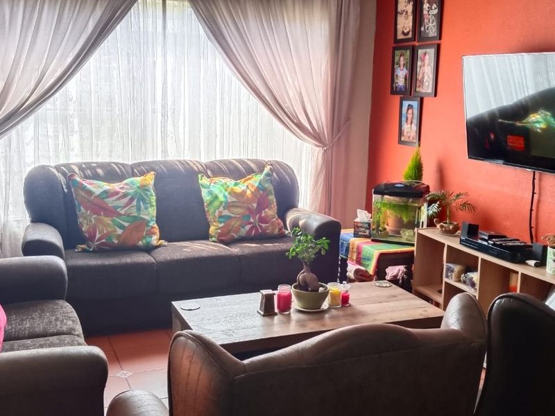 A comfortable living room featuring tiled flooring and large windows with curtains, providing a bright and functional space for relaxation.