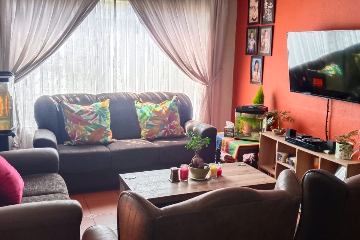 A comfortable living room featuring tiled flooring and large windows with curtains, providing a bright and functional space for relaxation.