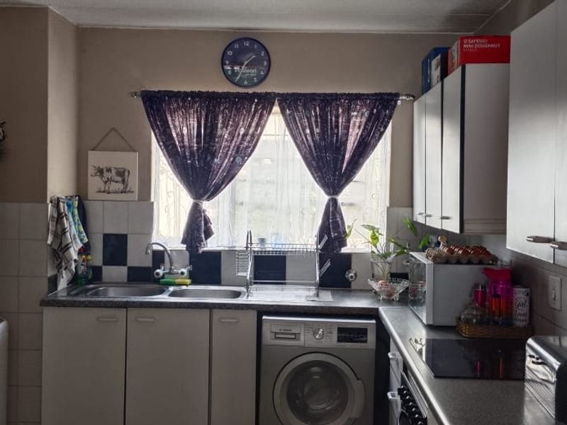 Functional kitchen featuring built-in cabinetry, double sink, electric hob, and integrated laundry appliance with tiled splashback.