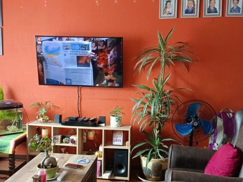 A living room area featuring a wall-mounted television and textured orange wall finish.