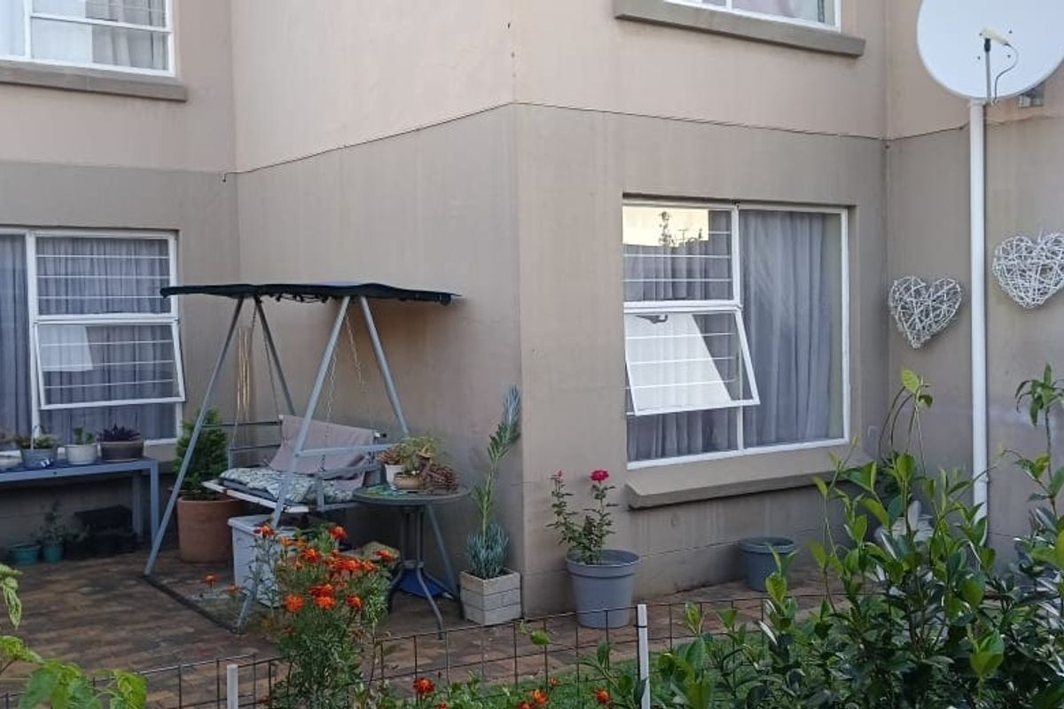 Ground floor apartment exterior featuring a paved patio area, security bars on windows, and exterior wall plastering.