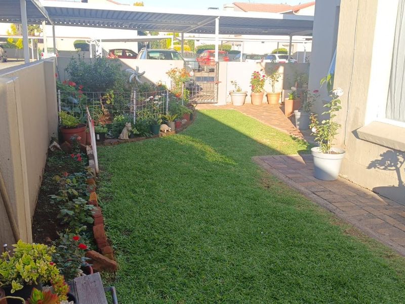 A private rear garden area featuring a well-maintained lawn, paved pathway, and boundary wall, adjacent to a covered carport structure.