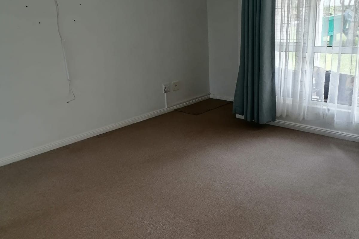 An empty living room featuring carpeted flooring, an installed air conditioning unit, and a sliding glass door leading to the exterior.