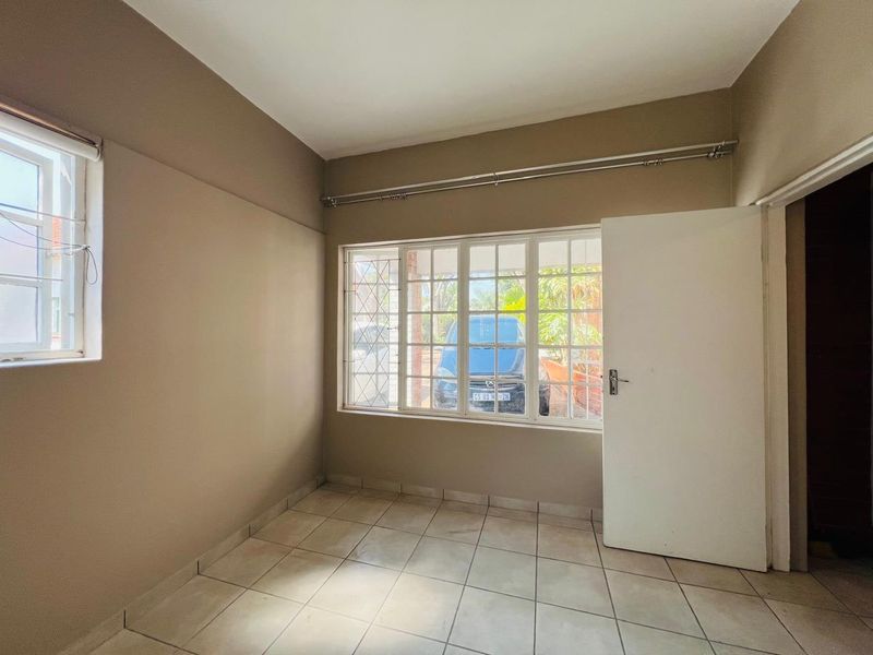 An empty bedroom featuring neutral wall paint, tiled flooring, and large windows with security bars, providing a blank canvas for personalization.