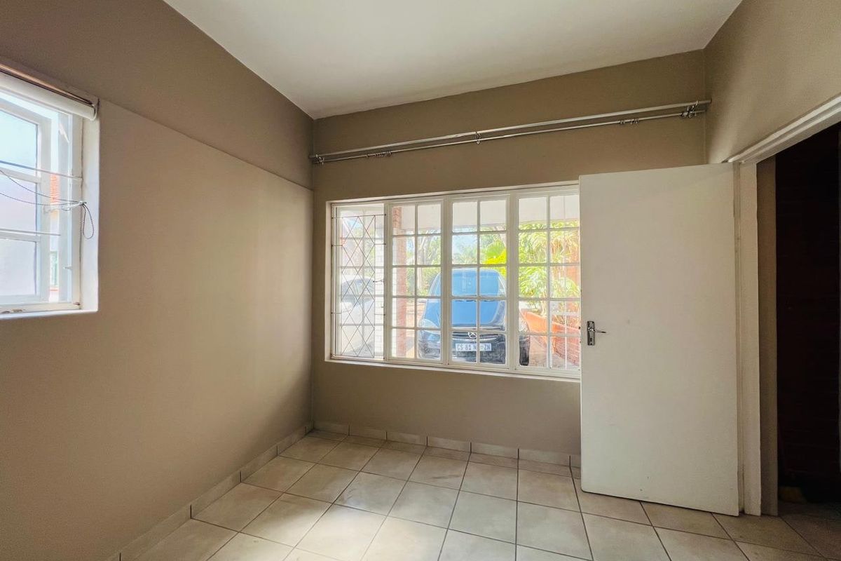 An empty bedroom featuring neutral wall paint, tiled flooring, and large windows with security bars, providing a blank canvas for personalization.