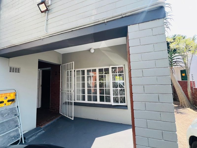Front entrance area featuring a paved patio, security gate, and white-framed windows set against a painted brick facade.