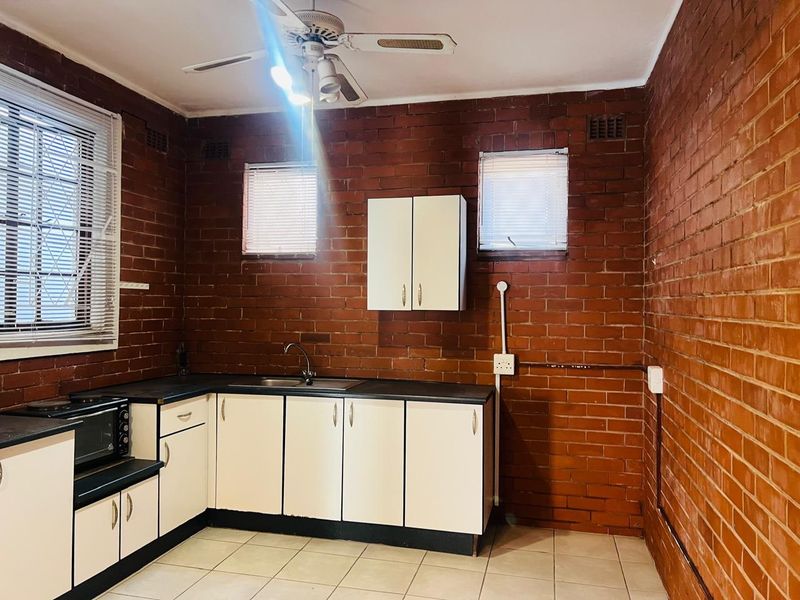 A functional kitchen featuring exposed brick walls, white cabinetry, tiled flooring, and a ceiling fan, offering a rustic aesthetic with potential for modernization.