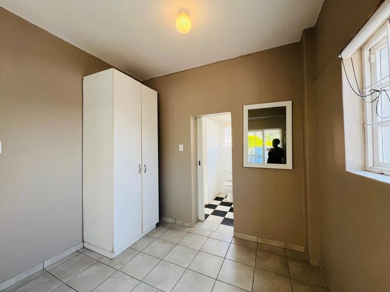 A simple, neutral-toned bedroom featuring tiled flooring, a built-in wardrobe, and direct access to an adjoining bathroom.
