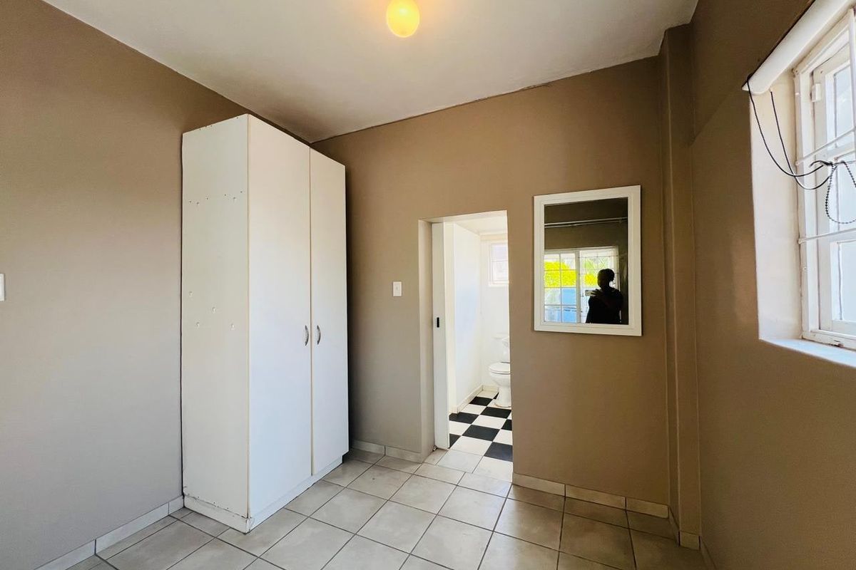A simple, neutral-toned bedroom featuring tiled flooring, a built-in wardrobe, and direct access to an adjoining bathroom.