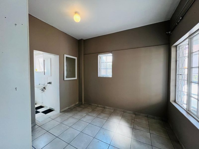 An empty bedroom featuring tiled flooring, leaded glass windows, and direct access to an en-suite bathroom with a checkered floor.